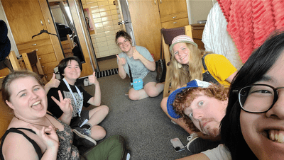 Group of six people sitting in a dorm roomhappily looking at the camera